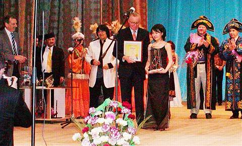 Zhanna Lee receives her framed certificate from a sponsor at the final gala presentation and concert. Jury members (right) receive traditional Kazakh garments and hats. To the left, Marat Bisengaliev (white jacket) and his manager Ganimat Bisengaliev (with yellow tie). Photo © 2004 Howard Smith